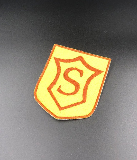 Shield shaped patch with a school emblem on it, a burnt umber trim, and golden yellow interior with an "S" in the center