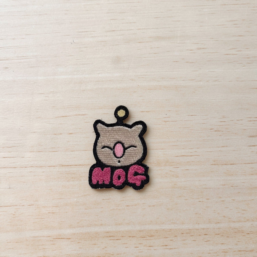 Embroidered patch with the face of a moogle from the Final Fantasy series, with the name "Mog" under it in pink