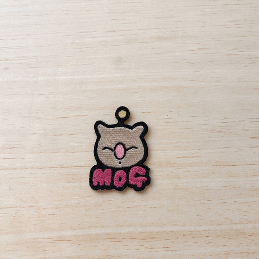 Embroidered patch with the face of a moogle from the Final Fantasy series, with the name "Mog" under it in pink