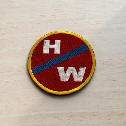 Circular patch with 'HW' on a red background with blue stripe, on a wooden surface