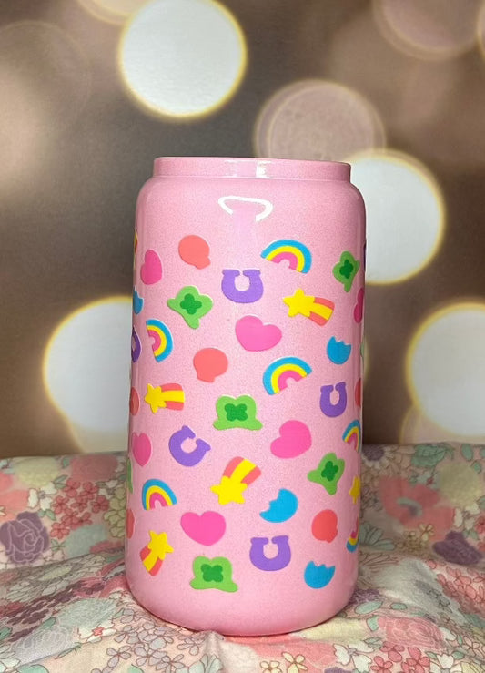 Pink opaque sparkly tumbler, covered with various charm designs. The charms are a pink balloon, pink heart, orange horse shoe, 3 color rainbow, shooting star and green top hat with a shamrock