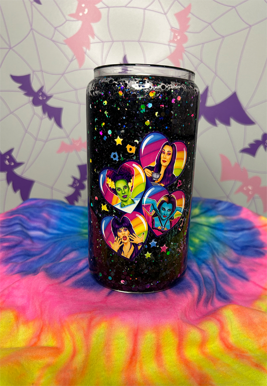 Glitter globe tumbler filled with black holographic glitter. On the front is a decal with 4 rainbow hearts, featuring Morticia Addams, Bride of Frankenstein, Lily Munster and Elvira in each heart
