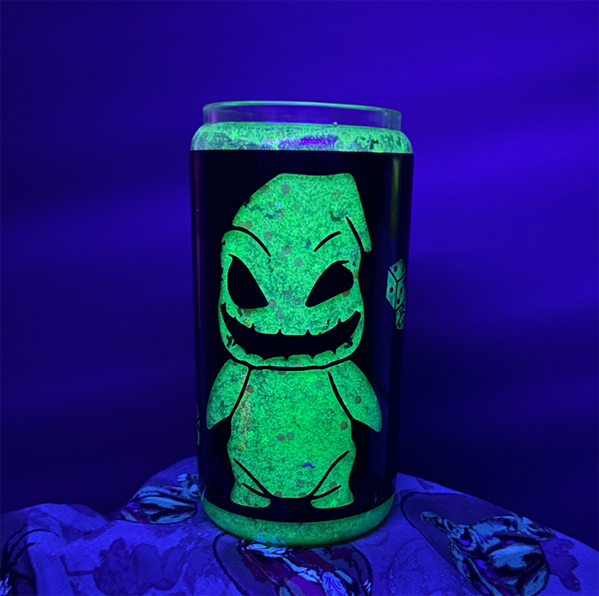 Glitter globe tumbler filled with neon green glitter under a black light to show it is glowing in the dark. Some black vinyl wrapped around it, with a cut out of Oogie Boogie from The Nightmare Before Christmas